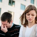 man-with-hand-squeezing-eyes-and-woman-looking-down-beside-him