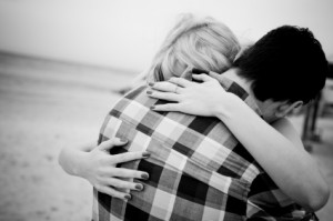 The back view of a couple embracing at the beach. No visible faces showing. Black and white image.